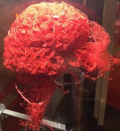 a red wig is on display in a glass case