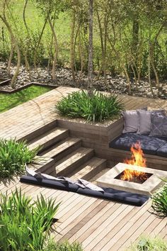 a fire pit in the middle of a wooden deck surrounded by greenery and trees