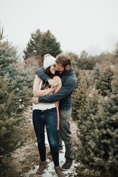 a man and woman hugging in the middle of a christmas tree farm filled with trees