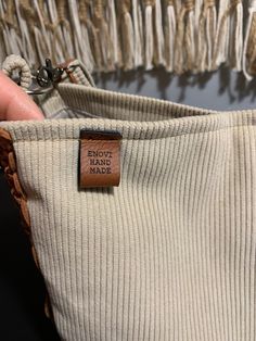 a person holding a small bag with a tag on it's side and some tassels hanging from the back