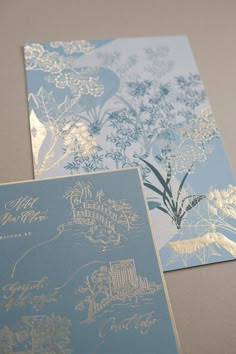 two blue and gold wedding cards with floral designs on the front, one in light blue