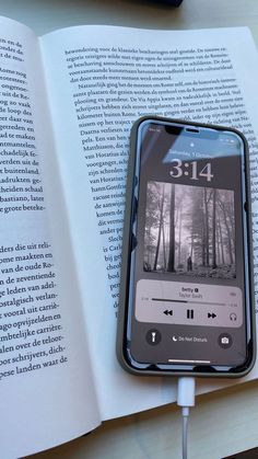 an open book with headphones attached to it next to a cell phone and ear buds