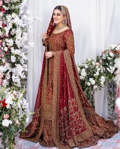 a woman in a red and gold bridal gown standing next to a floral arch