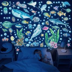 a child laying in bed under a wall mural with sea animals and fish on it