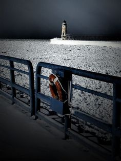 a horse is tied to a fence in the snow near a light house at night