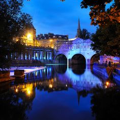 a bridge over a body of water with buildings in the background at night and lit up by street lights