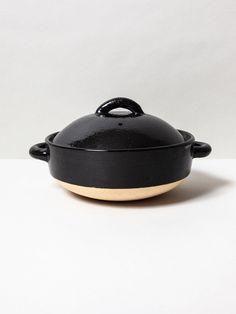 a black casserole on a white surface with a wooden lid and handle in the shape of an oval