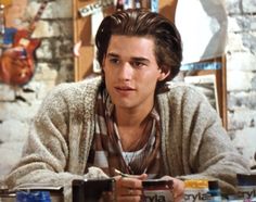 a young man sitting at a table holding a cup