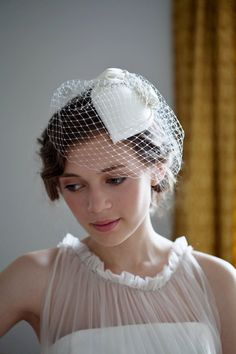 a woman in a white dress wearing a veil and headpiece with a flower on it