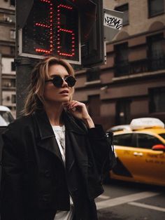 a woman wearing sunglasses standing next to a street sign with the word 24 on it