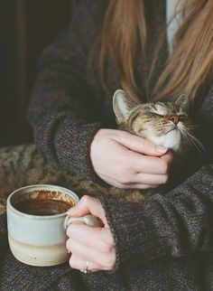 a woman holding a cat in her arms next to a cup of coffee