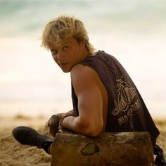 a young man sitting on top of a wooden log