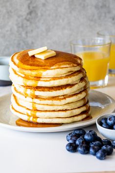 a stack of pancakes on a plate with blueberries and orange juice in the background