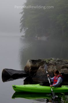 a person in a kayak paddling on the water near some rocks and trees