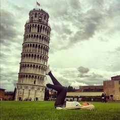 a woman laying on the ground in front of a leaning tower