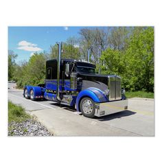 a blue semi truck parked on the side of the road in front of some trees