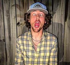 a man with his mouth wide open in front of a wooden wall wearing a hat