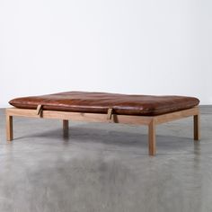 a wooden bench with brown leather cushions on it's sides and two legs, in front of a white wall