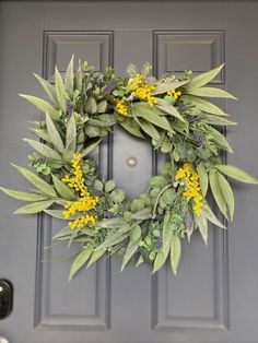 a wreath with yellow flowers and green leaves hangs on the front door's gray door