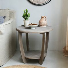 a small table with a vase and potted plant on it in front of a large clock