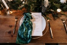 a place setting with napkins and silverware on a wooden table surrounded by greenery