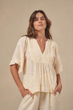 The Tulum top from Australian brand Little Lies is a perfect staple for spring/summer. Features pleated detail on the front, a flattering square sleeve and a v-neckline. This gorgeous top is an oversized fit that can be paired with your favorite pants or shorts. Semi-sheer. Materials: 100% Cotton Care: Wash with like colors; cold gentle machine wash; do not bleach; lay flat to dry; warm iron; do not tumble dry. Size Info: Model is 5'8" and is wearing a size S; relaxed fit Size Guide | Shipping Policy Casual Short Sleeve V-neck Top For Brunch, Versatile V-neck Blouse For Beach, Relaxed V-neck Blouse For Day Out, Versatile Beige V-neck Blouse, Spring Top With Notched Neckline For Day Out, Beige V-neck Summer Top, Effortless V-neck Blouse For Day Out, Beige V-neck Top For Summer, Chic Split Neck Top For Day Out