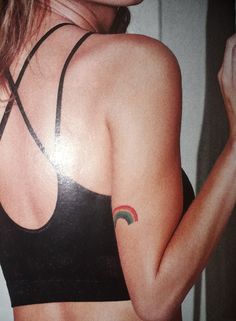 a woman with a rainbow tattoo on her arm and shoulder, wearing a black sports bra top