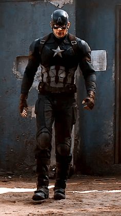 a man dressed as captain america walking in front of a blue building with an open door