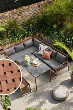 an outdoor seating area with grey cushions and pillows on the floor, surrounded by greenery