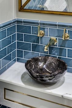 a bowl shaped sink sits on a counter in front of a blue tiled wall and gold faucet