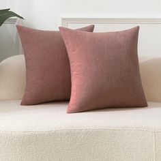 two pink pillows sitting on top of a white couch next to a potted plant