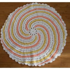 a crocheted doily on a wooden floor with an orange, yellow and white design