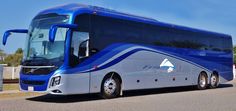 a blue and silver tour bus parked on the side of the road with trees in the background