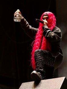 a woman with pink hair is holding a bottle and singing into a microphone on stage