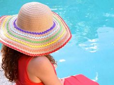 a woman wearing a colorful hat sitting next to a swimming pool with her back to the camera