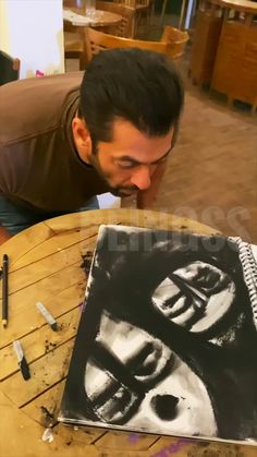 a man is looking at a drawing on a wooden table in front of his face