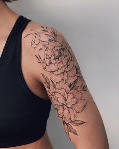 a woman's arm with flowers on it and a black tank top underneath her