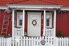 a white picket fence sitting in front of a red house with a wreath on it