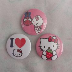 three hello kitty buttons on a white sheet with red heart and spiderman in the background