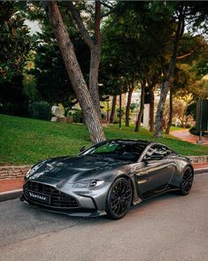 a grey sports car parked on the side of the road next to trees and grass