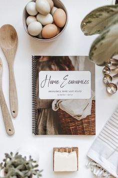 an open book sitting on top of a table next to some eggs and spoons