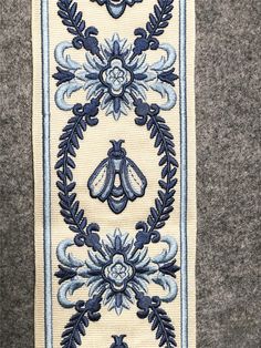 a blue and white embroidered design on a gray background, with an insect in the center