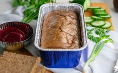 a loaf of bread sitting in a tin next to some crackers and cucumbers