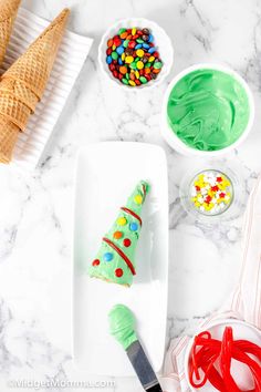 an ice cream cone decorated like a christmas tree on a white plate next to bowls of candy