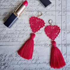 two red tasselled earrings on top of a piece of paper with lipstick next to it