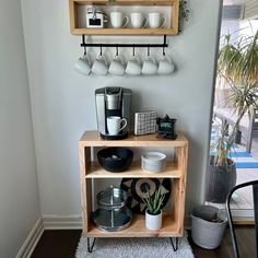 a shelf with cups and plates on it in the corner of a room next to a potted plant