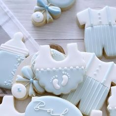 cookies decorated with blue and white icing are on a wooden table next to baby bibs