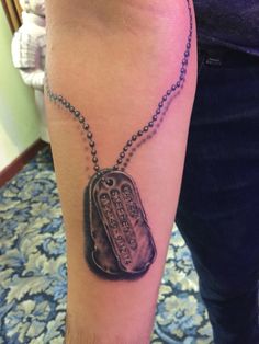 a person with a tattoo on their arm has a dog tag attached to the chain