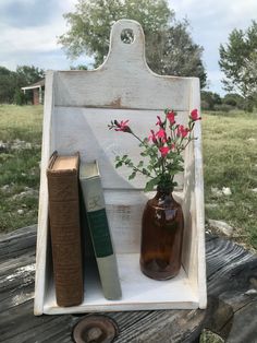 a vase with flowers and books is sitting on an old wooden crate in the grass