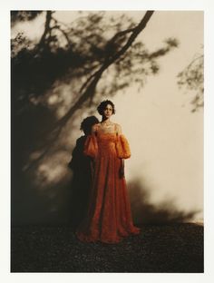 a woman in an orange dress standing next to a tree with her shadow on the wall